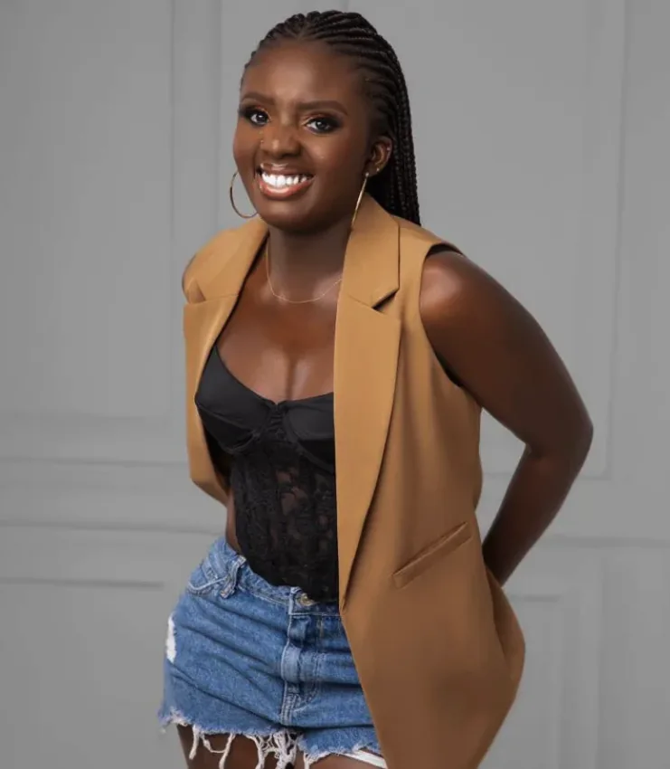 DJ Akuaa smiling in a tan vest and denim shorts